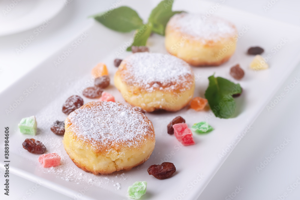 Curd pancakes with raisins and candied fruits on a white plate, top view Curd pancakes with raisins and candied fruits on a white plate, top view