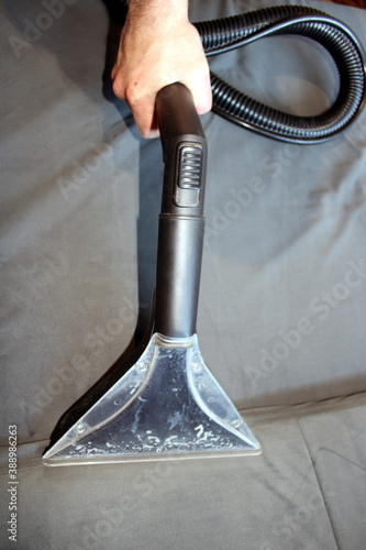 The man's hand makes the dry cleaning of the gray sofa with a cleanser.