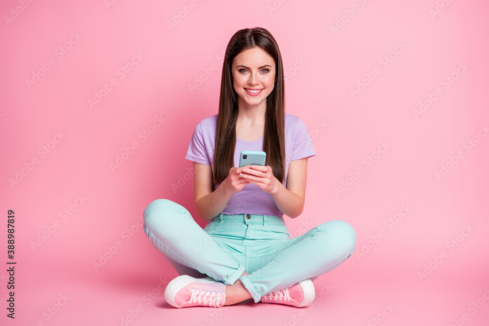 Full size photo of positive cheerful girl sit floor legs crossed use cellphone enjoy social network communication wear teal purple pants isolated over pastel color background Full size photo of positive cheerful girl sit floor legs crossed use cellphone enjoy social network communication wear teal purple pants isolated over pastel color background