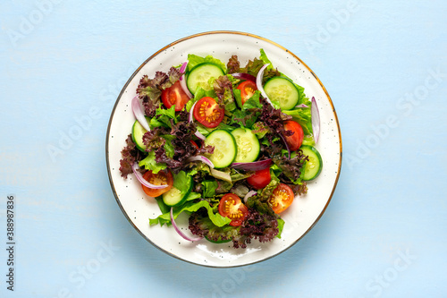 Healthy vegetable salad of cherry tomatoes, cucumber slices, green and purple lettuce leaves, onions and olive oil in plate on blue wooden table Top view Flat lay Diet, mediterranean menu Vegan food