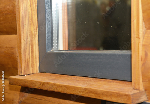 A wooden window sill with a upvc plastic window installed in a house with log siding panels facade.