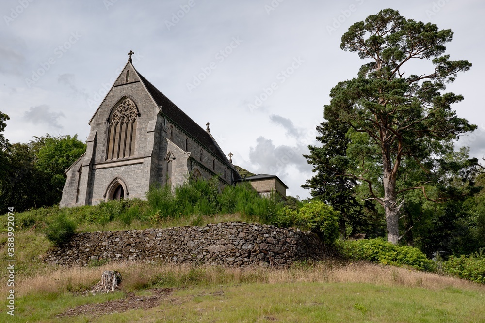 Old Saint Mary & Saint Finnan Catholic Church on a hill with a green tree in Glenfinnan, Scotland
