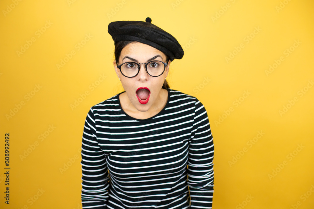 Young beautiful brunette woman wearing french beret and glasses over yellow background afraid and shocked with surprise and amazed expression, fear and excited face. Young beautiful brunette woman wearing french beret and glasses over yellow background afraid and shocked with surprise and amazed expression, fear and excited face.