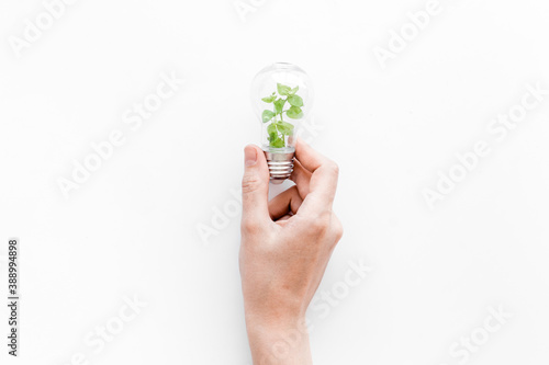 Hand holds light bulb with grass inside - green energy concept, top view