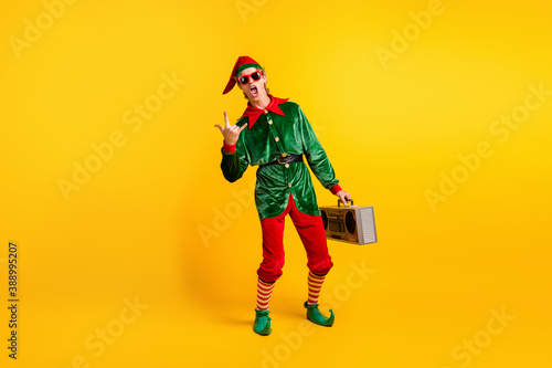 Full length body size view of his he nice attractive crazy naughty cheery funny guy elf carrying player having fun showing horn symbol isolated over bright vivid shine vibrant yellow color background