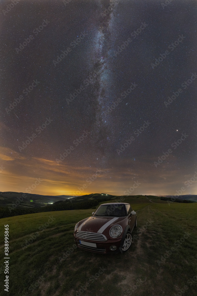 Car on a meadow, a dirt road under the night sky with the Milky Way