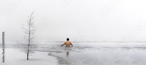 Man going ice swimming into a frozen lake in winter panorama photo