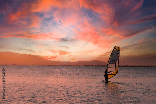 Windsurfer riding on a surfboard against a cloudy orange sunset. Empty copy space for Editor's content.