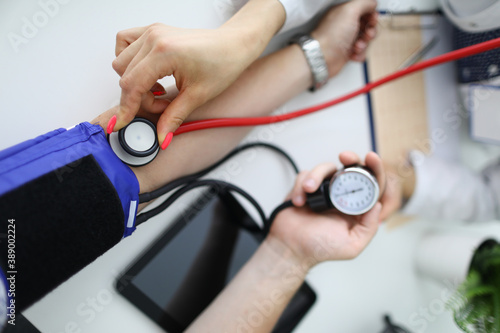 Cardiologist with red stethoscope measures blood pressure of patient in clinic closeup. Diagnosis of diseases of cardiovascular system concept.