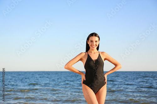 Beautiful young woman in black stylish swimsuit on beach. Space for text