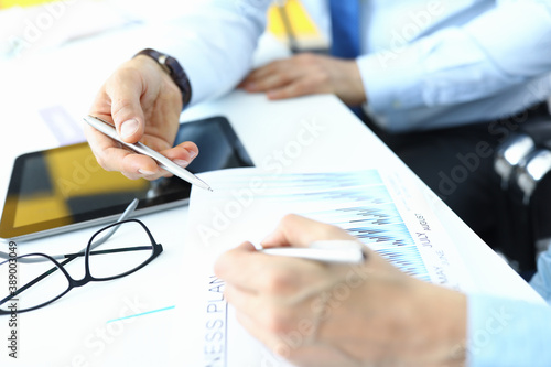 Male and female hands with ballpoint pens over document with plan and tablet at table in office closeup. Business planning concept.