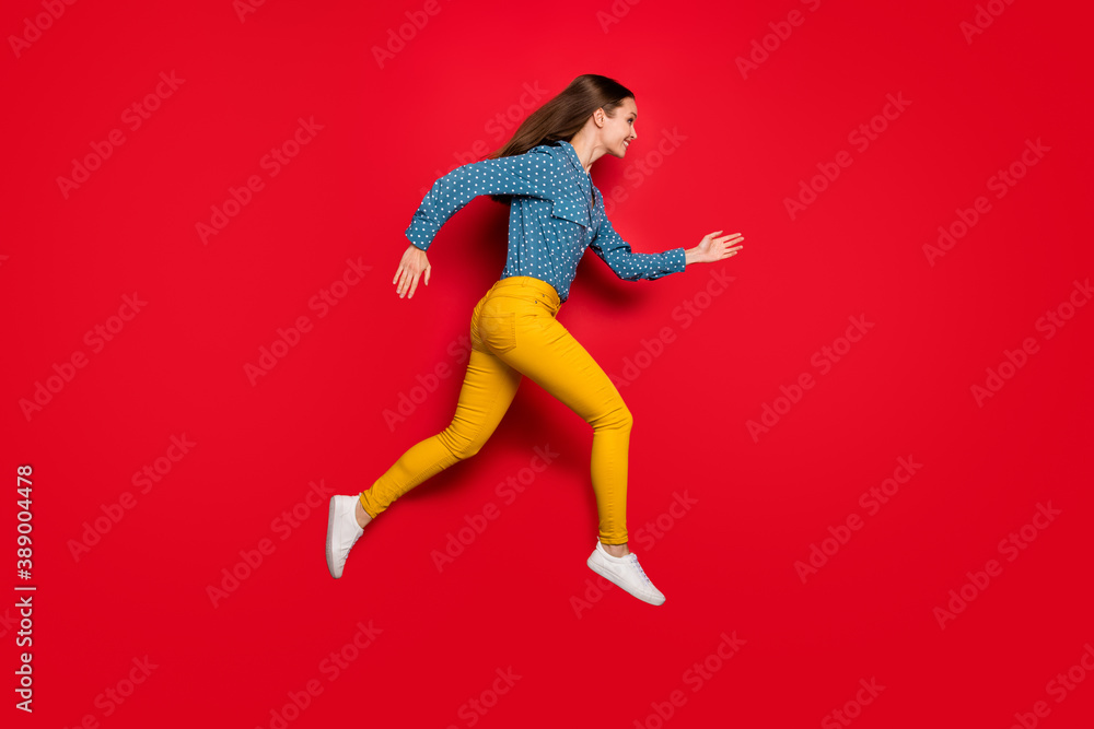 Full length body size profile side view of pretty cheerful slender girl jumping running activity isolated on bright red color background