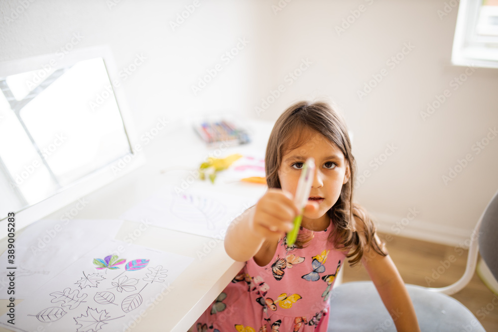 Little girl next to a table with coloring leaves images shows a pen