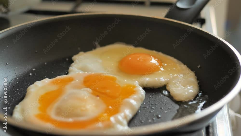 Cooking delicious fresh chicken eggs on modern frying pan with hot oil on stove at bright light in kitchen extreme close view Cooking delicious fresh chicken eggs on modern frying pan with hot oil on stove at bright light in kitchen extreme close view