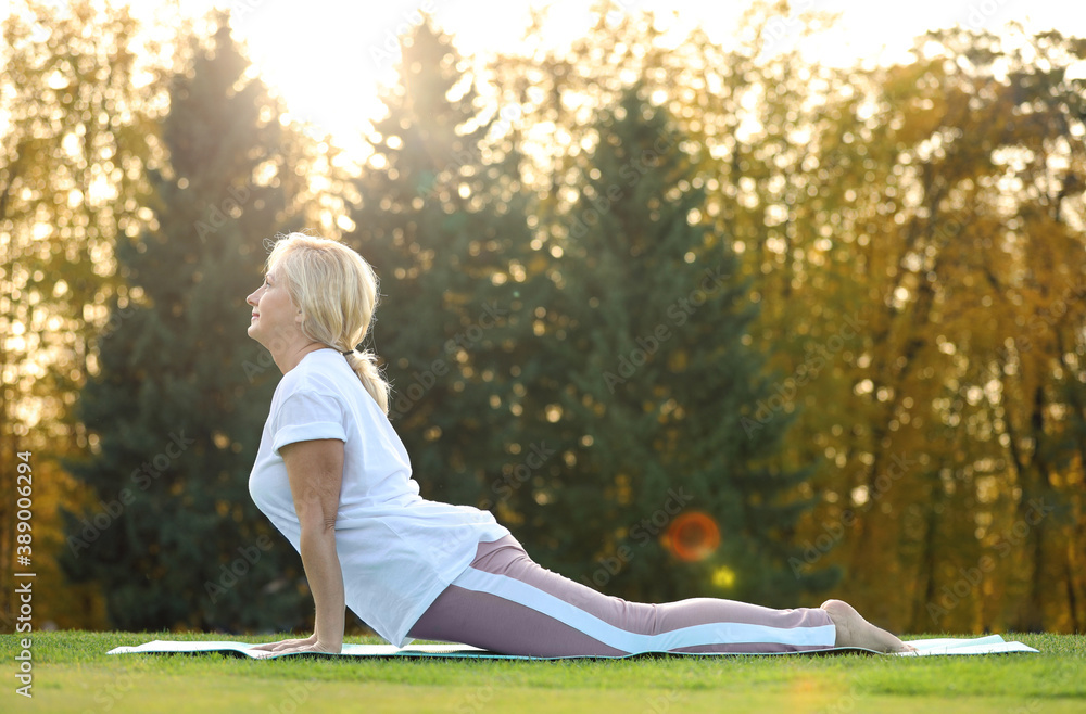 Mature woman practicing yoga on green grass in park Mature woman practicing yoga on green grass in park
