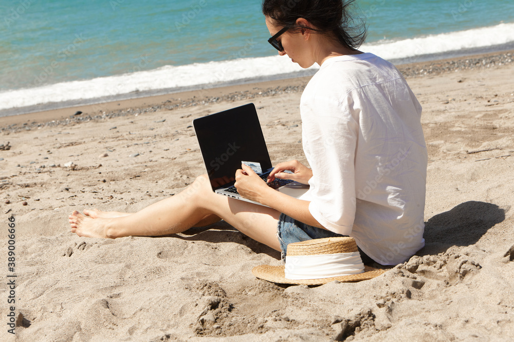 Young woman using laptop computer on a beach. Vacation lifestyle communication. Holds a Bank card in his hands. The concept of online shopping or online shopping