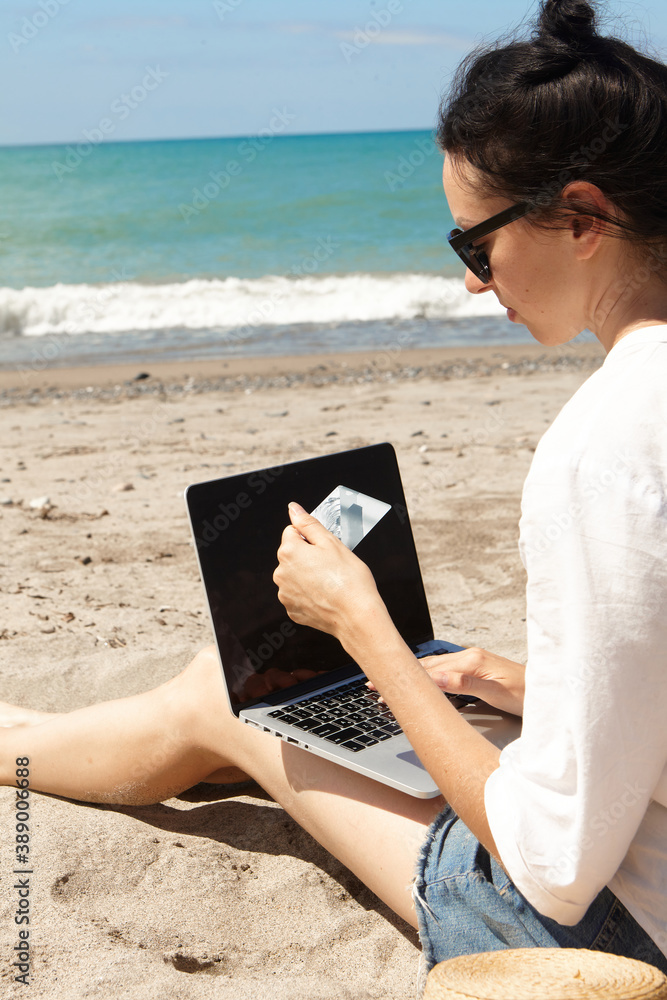 Young woman using laptop computer on a beach. Vacation lifestyle communication. Holds a Bank card in his hands. The concept of online shopping or online shopping