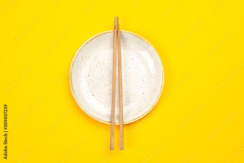 Empty plate and chopsticks on yellow background Empty plate and chopsticks on yellow background