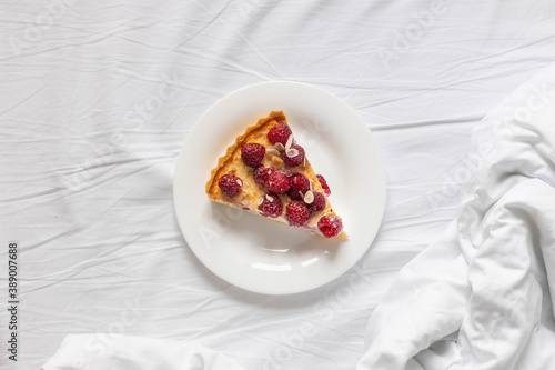 Piece of classic cheesecake with raspberry berries on a white plate on the bed.