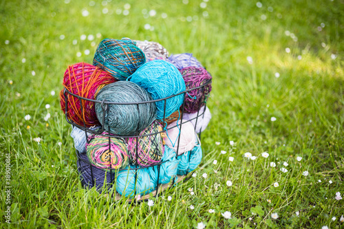 Colorful balls of woolen yarn in a metal basket on the grass