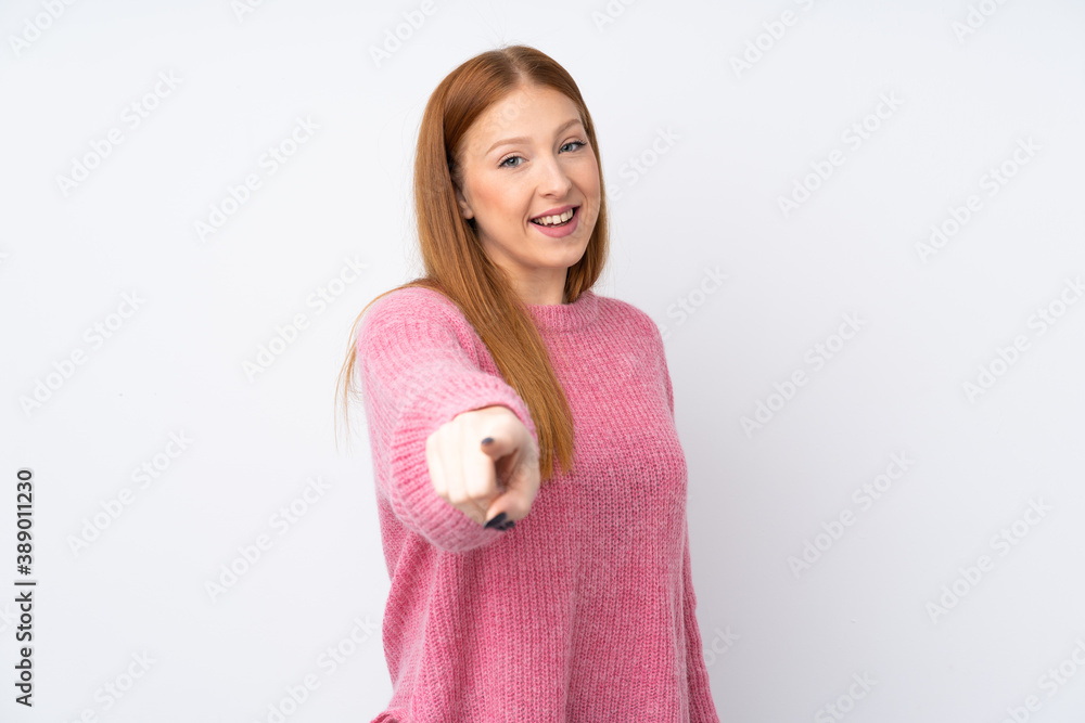 Young redhead woman with pink sweater over isolated white background points finger at you with a confident expression Young redhead woman with pink sweater over isolated white background points finger at you with a confident expression