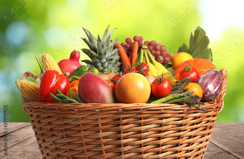 Fresh organic fruits and vegetables in wicker basket on wooden table  closeup