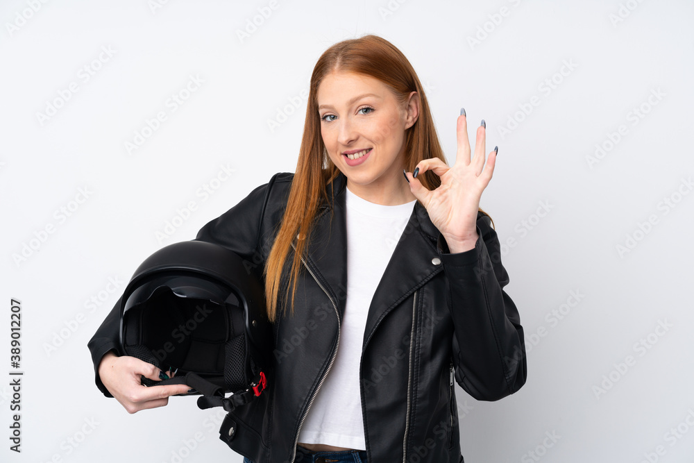 Young redhead woman with a motorcycle helmet over isolated white background showing ok sign with fingers Young redhead woman with a motorcycle helmet over isolated white background showing ok sign with fingers