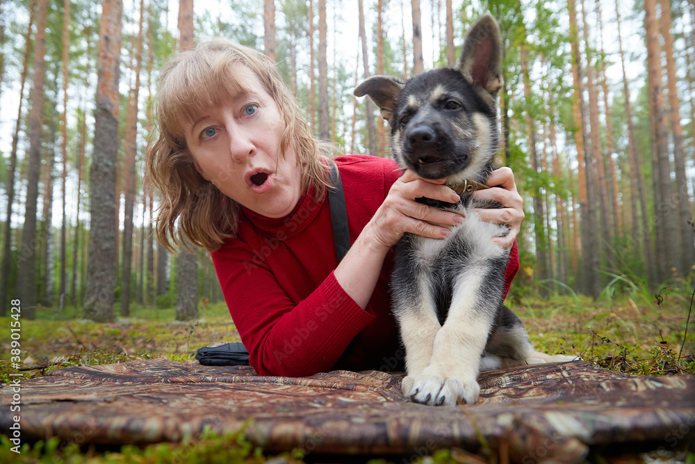 A girl in a red sweater playing with a small German shepherd puppy in the woods A girl in a red sweater playing with a small German shepherd puppy in the woods