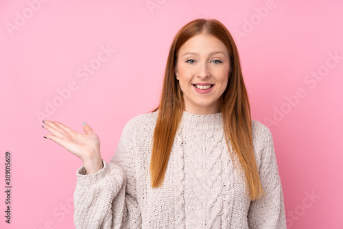 Young redhead woman over isolated pink background holding copyspace imaginary on the palm to insert an ad