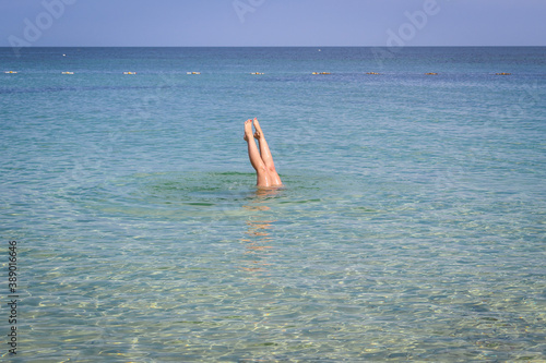 A woman plunging in turquoise sea water. Feet sticking out of the water.