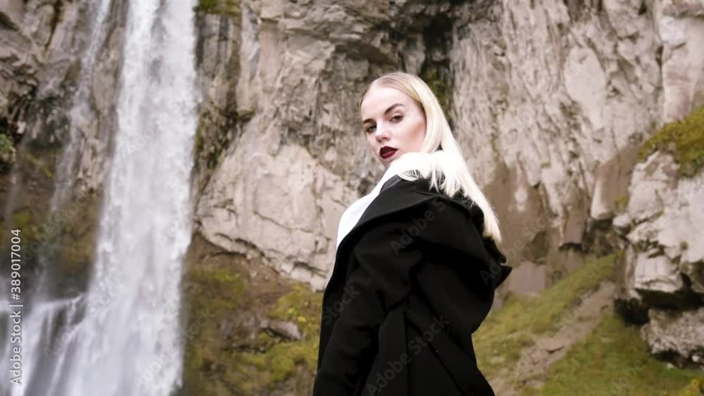 Beautiful blonde woman on the background of a large waterfall high in the mountains in autumn, beautiful autumn scenery and mountain views. Video in HD quality Beautiful blonde woman on the background of a large waterfall high in the mountains in autumn, beautiful autumn scenery and mountain views. Video in HD quality