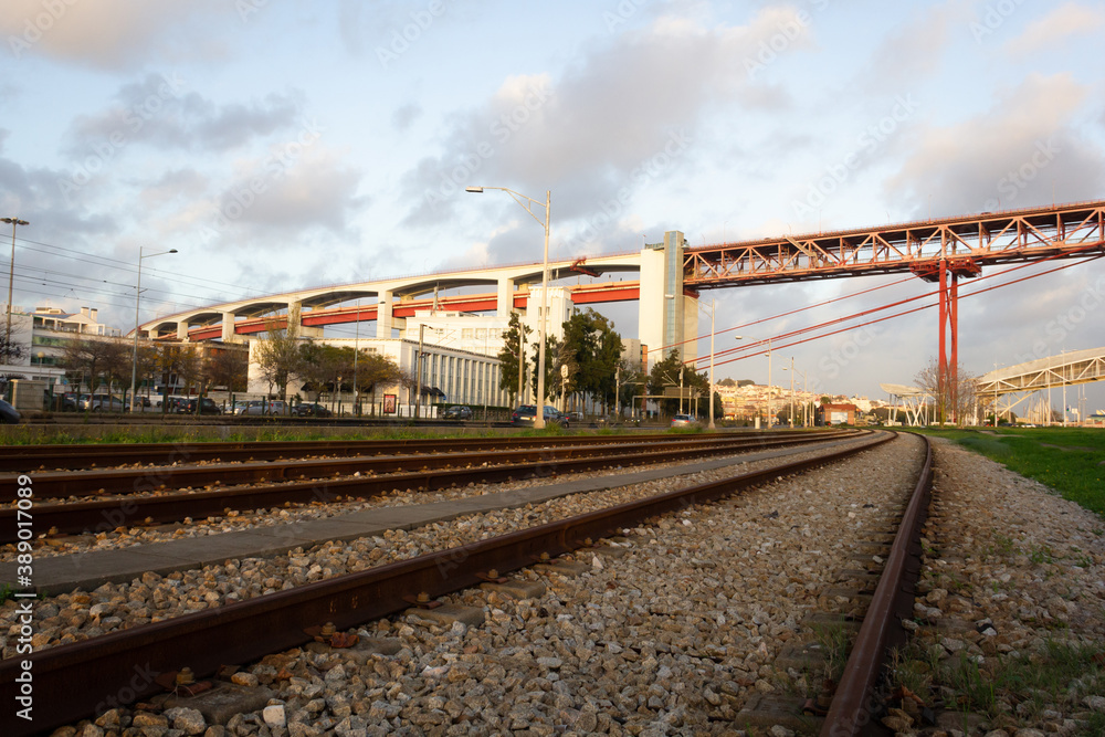 Train tracks leading to April 25 Bridge at sunset in Lisbon. Railway  by iconic landmark of Portugal capital