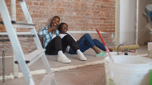 African couple sitting on floor in empty room of new home planning design photo