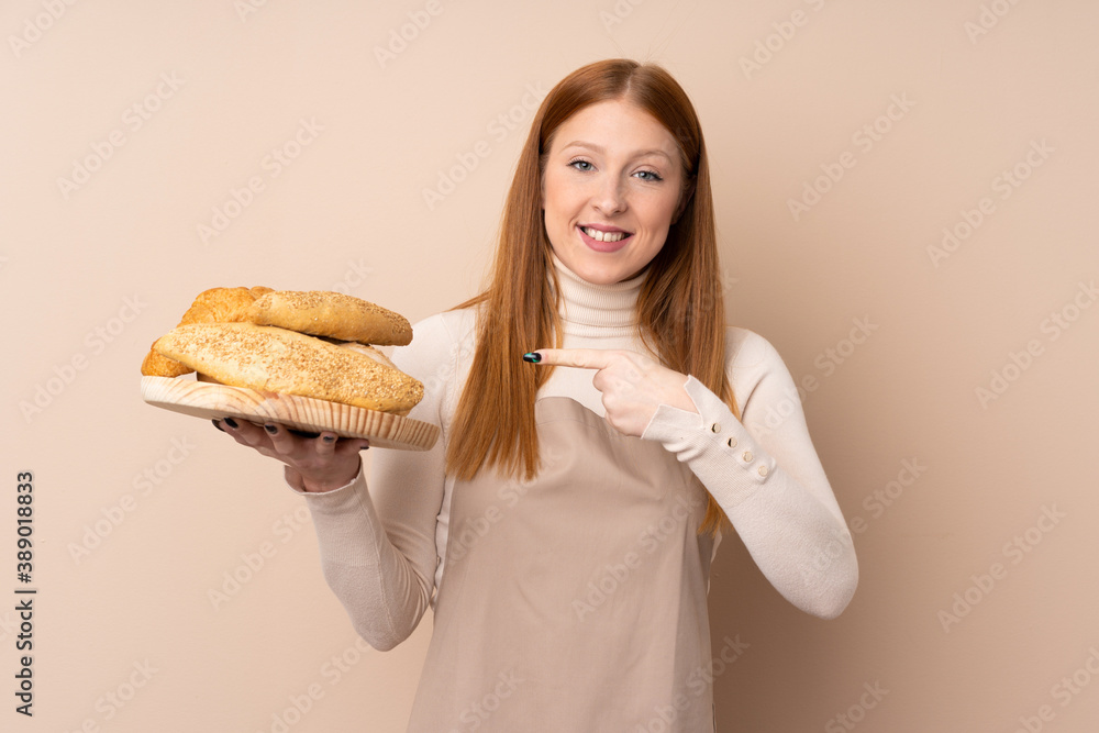 Young redhead woman in chef uniform. Female baker holding a table with several breads and pointing it Young redhead woman in chef uniform. Female baker holding a table with several breads and pointing it