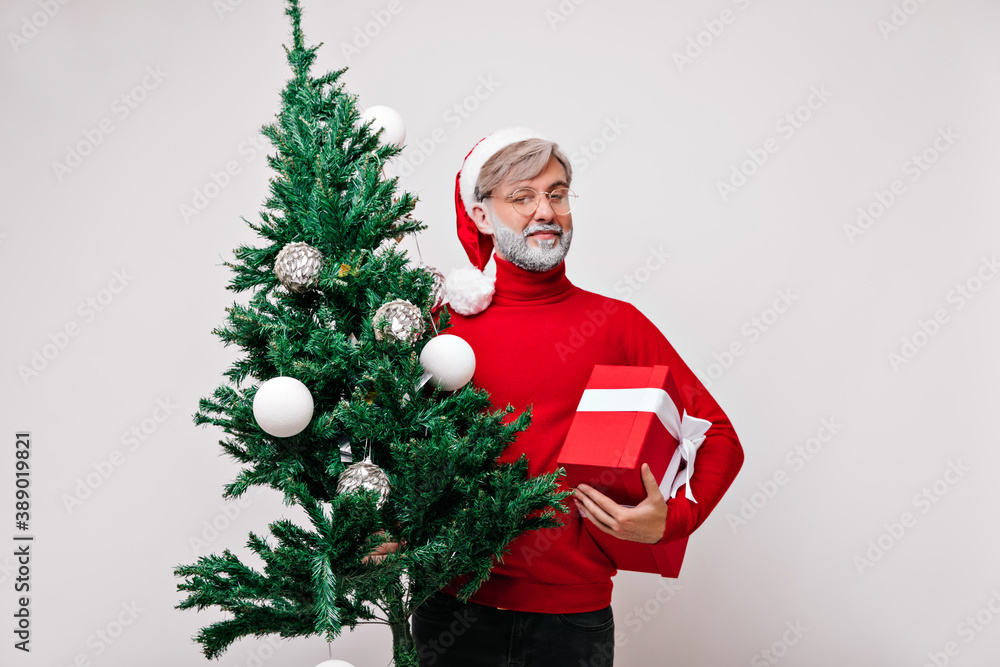 Carefree old man with white beard holding new year present. Cheerful santa claus posing with little christmas tree. Carefree old man with white beard holding new year present. Cheerful santa claus posing with little christmas tree.