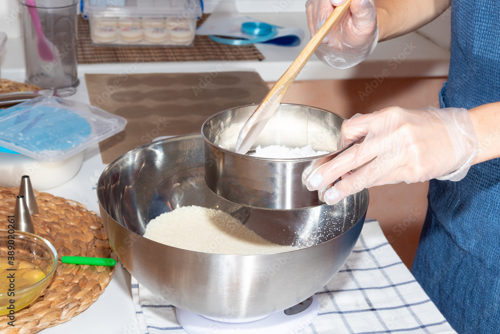 Using a sieve and a wooden spatula, the girl sifts the flour. Cooking process. Using a sieve and a wooden spatula, the girl sifts the flour. Cooking process.