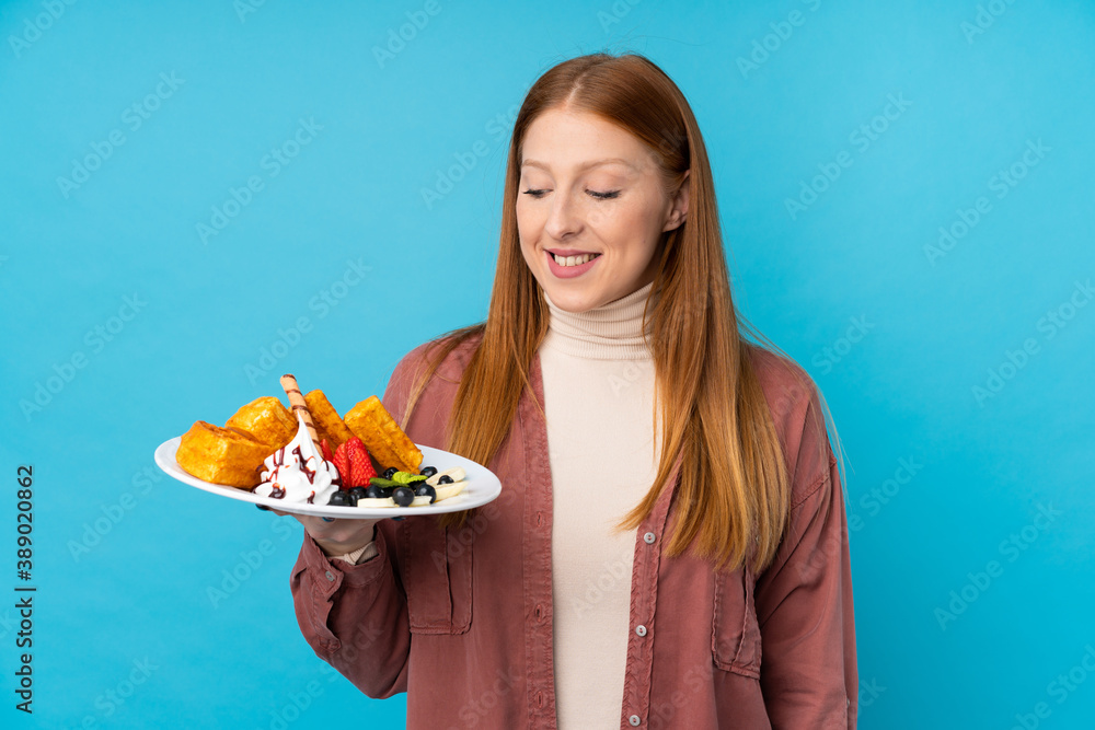 Young redhead woman holding waffles over isolated background with happy expression Young redhead woman holding waffles over isolated background with happy expression