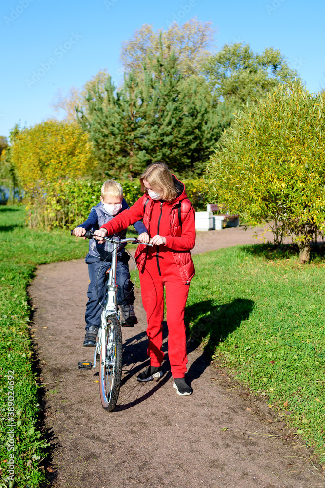 Naklejka premium Mother and son in the foreground in the autumn Park in a medical mask.