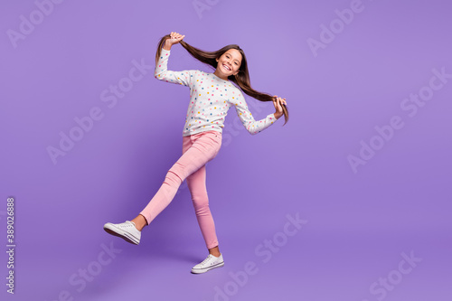 Fototapeta Naklejka Na Ścianę i Meble -  Full length body size photo little girl smiling happily keeping long hair tails kicking dancing isolated on bright violet color background