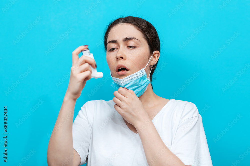 Asthma. Portrait of young woman takes a medical mask to make the inhalation of medication. Light blue background Asthma. Portrait of young woman takes a medical mask to make the inhalation of medication. Light blue background
