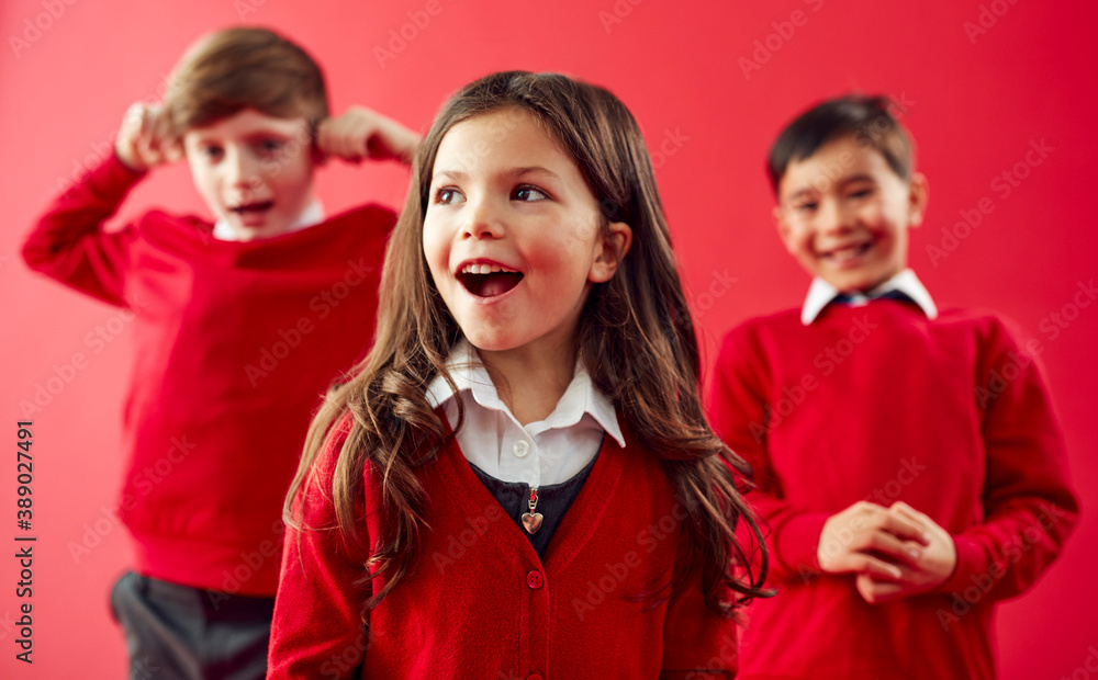 Group Of Excited Elementary School Pupils Wearing Uniform Having Fun Against Red Studio Background
