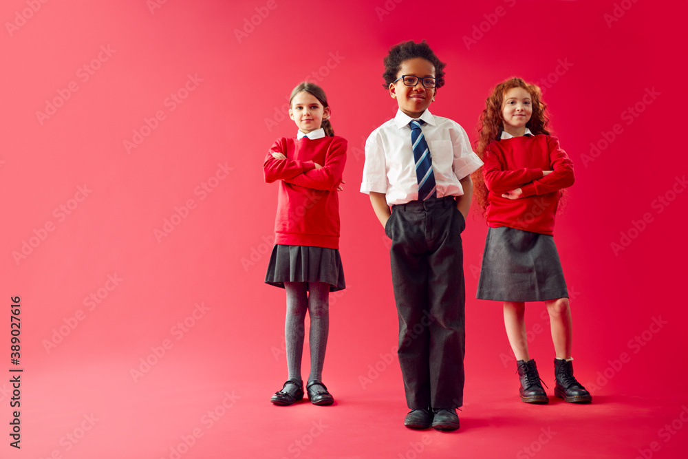 Group Of Elementary School Pupils Wearing Uniform Folding Arms Against Red Studio Background Group Of Elementary School Pupils Wearing Uniform Folding Arms Against Red Studio Background