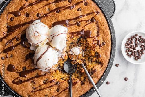 Skillet cookie with scoops of vanilla ice cream on a white marble background with drops of chocolate