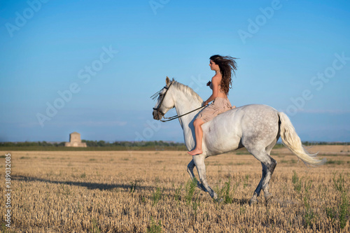Attractive young Caucasian female with a beautiful dress riding a horse in the countryside
