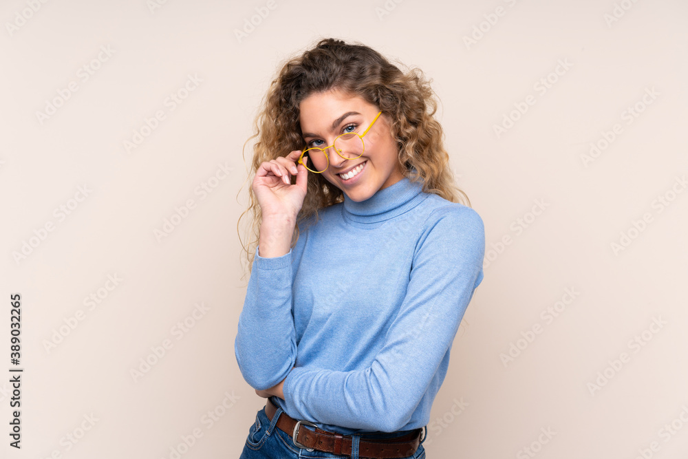 Young blonde woman with curly hair wearing a turtleneck sweater isolated on beige background with glasses and smiling Young blonde woman with curly hair wearing a turtleneck sweater isolated on beige background with glasses and smiling