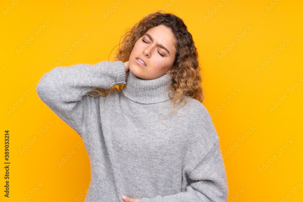 Young blonde woman with curly hair wearing a turtleneck sweater isolated on yellow background with neckache