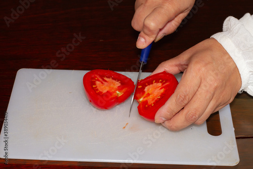 Woman cutting tomato on plastic board, healthy food, vegan food, seitan photo