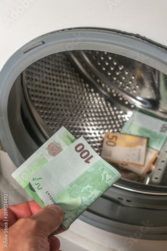 Money laundering concept, a man hand adding the 100 euro banknote into a pile of euro banknotes to be cleaned inside the washing machine, background, details.