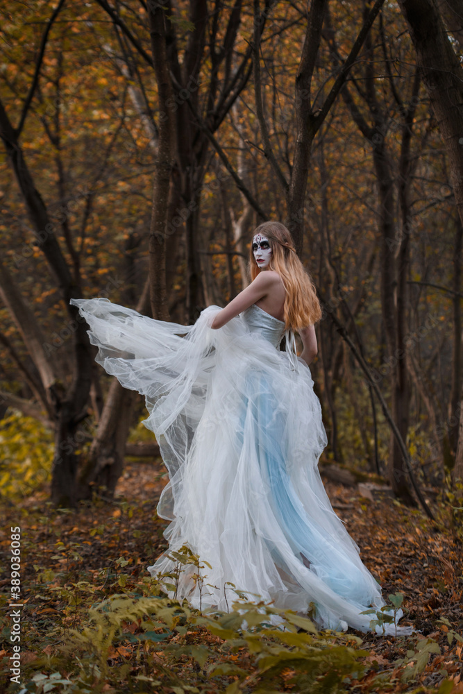 A girl bride with a terrible make-up on her face in a long white dress in the autumn forest.