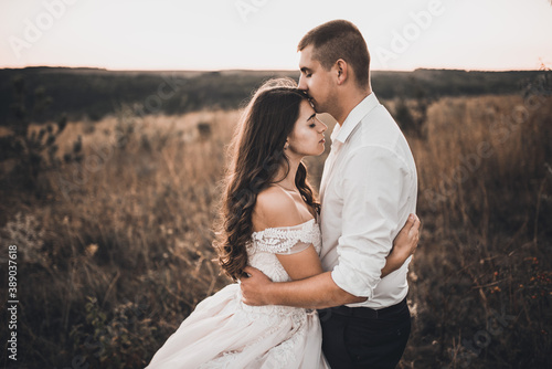 bride and groom in wedding white dress walking on the meadow in summer at sunset